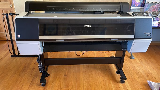 An Epson SureColor large-format printer sits on a wheeled stand on a hardwood floor.