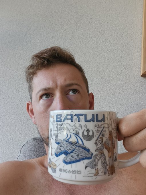 A man looks upward while holding a white Star Wars mug that reads 'BATTUU' and 'SKYHD' with illustrations of characters and spaceships.