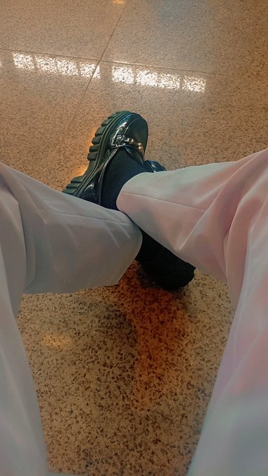 A first-person view of black chunky boots paired with white wide-leg pants, standing on a speckled terrazzo floor.