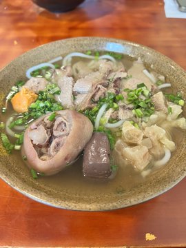 A bowl of noodle soup is garnished with meat, a bone-in piece, and chopped green onions.