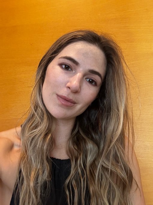 A woman with long, wavy highlighted hair poses against a warm orange wall, looking relaxed and refreshed. The image likely showcases the glowing, healthy skin results following a media-spa treatment in Seoul, illustrating the benefits mentioned in her caption.
