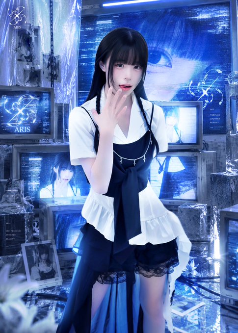 A young woman with long dark hair poses in a gothic-style blue and white outfit with lace shorts, standing before a backdrop of stacked monitors displaying the "ARIS" logo and her own image, with one monitor labeled "TOPOLOGICAL" and "REALITY." The post's "ARIS" text and "@ARIS__COCO" handle directly correspond to the branding visible throughout the image.