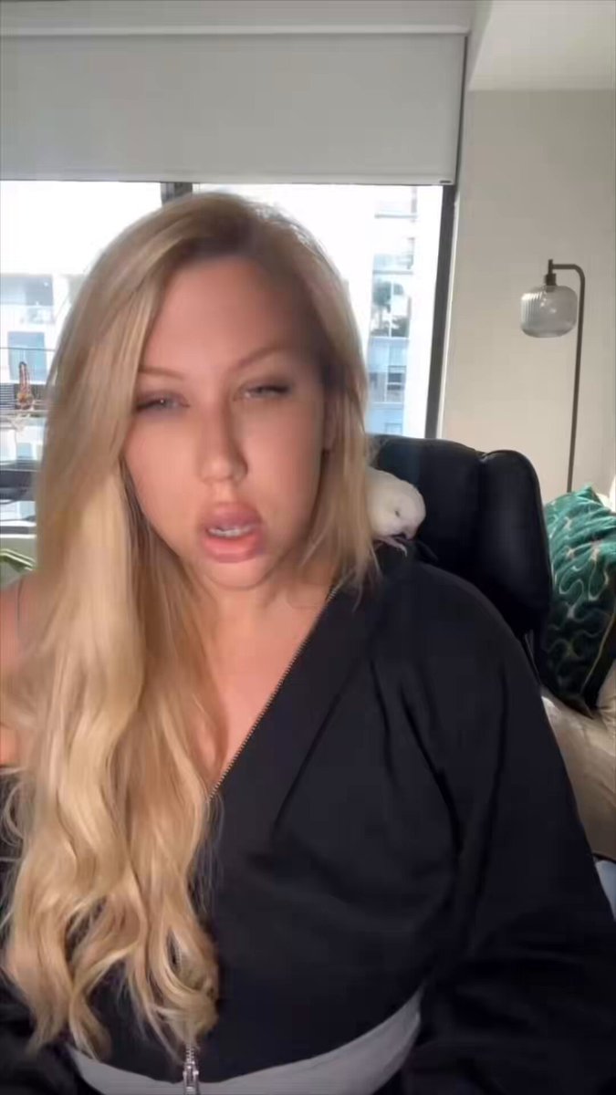 In the image, a woman with blonde hair wearing a black outfit is sitting down and talking into a microphone. She appears to be engaged in a conversation or presentation. The background of the image features a window that allows natural light to enter the room. There are also two birds visible in the scene - one on the left side of the frame, and another bird slightly behind it. The text "The limited edition BONK x Ledger Nano S Plus is almost sold out after @amystreet 's Bird unboxed his." suggests that there might be a connection between the woman's outfit or appearance and the birds in the image.