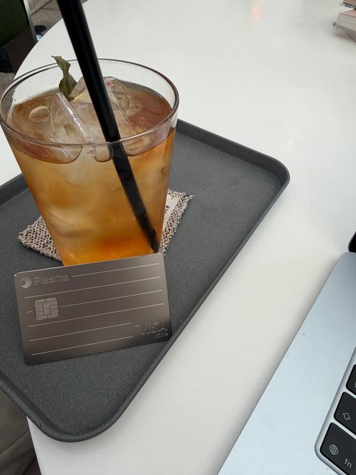 A glass of iced tea with a black straw sits on a dark tray next to a laptop, accompanied by a 'Flasma' credit card.