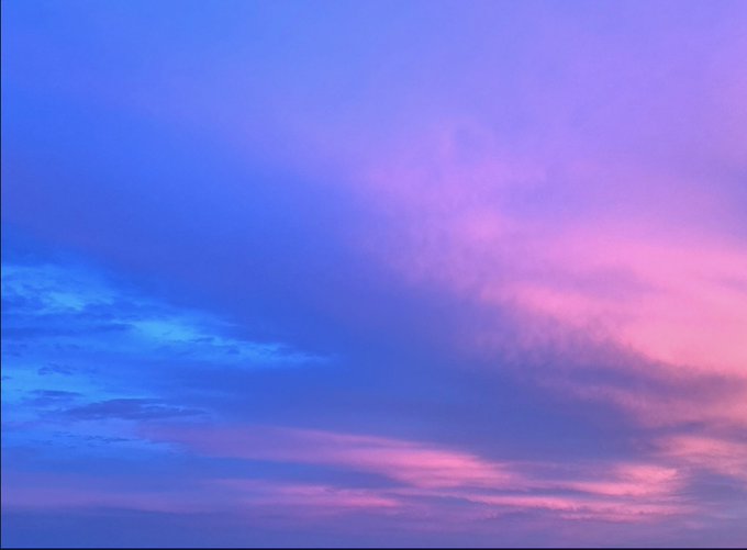 A serene sky transitioning from deep blue on the left to soft pink and purple hues on the right, with wispy clouds scattering across the frame.