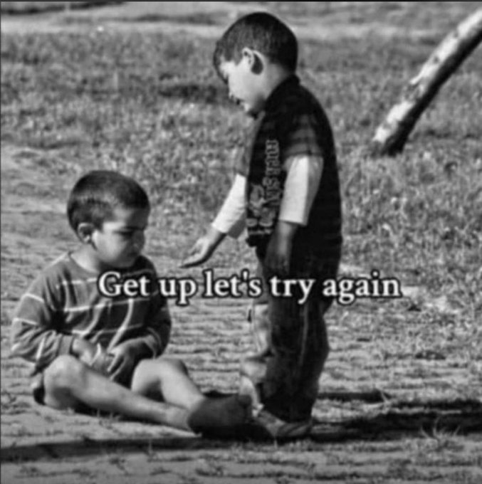 A black and white meme image showing two young boys, with the standing boy reaching down to help the seated boy up, captioned 'Get up let's try again'.