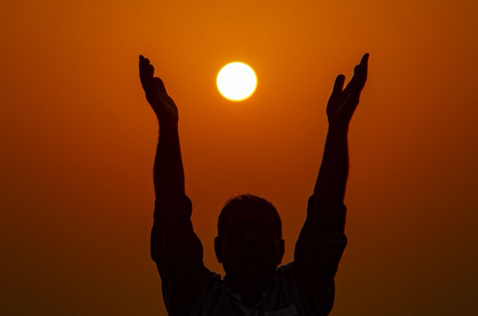 A silhouetted figure raises both arms toward a glowing orange sun, as if trying to grasp it in mid-air—capturing the wistful "wish to stop time and hold the sun" described in the caption.