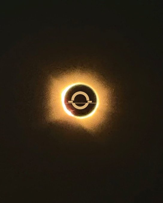 A glowing ring of golden light pierces the darkness around a dark circular shape, with a stylized "C" symbol faintly visible at its center—capturing the dramatic "totality" phase of a solar eclipse.