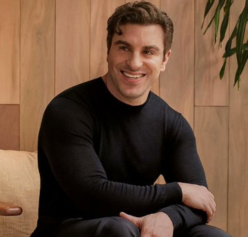 A smiling man in a black sweater sits on a couch against a wood-paneled wall, identified by the accompanying post as Airbnb CEO Brian Chesky, whose X account was reportedly hacked to post about real world asset tokenization.