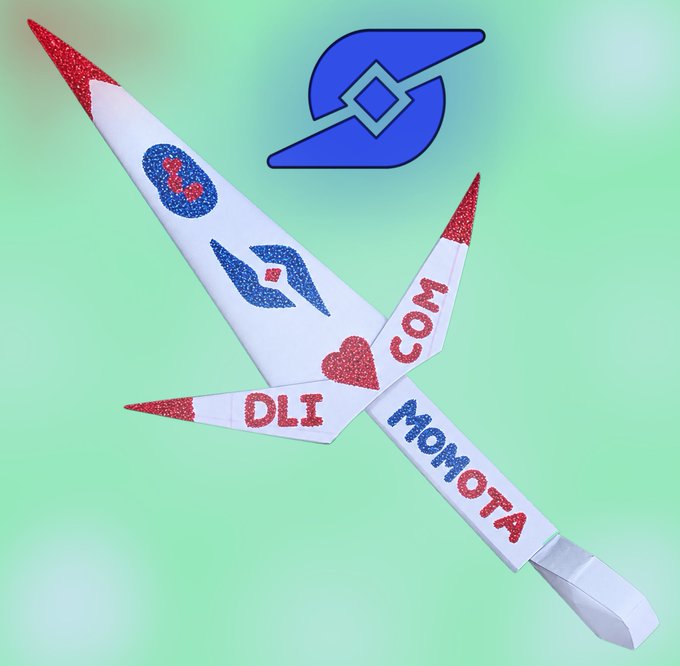 A paper origami plane decorated with red and blue glitter, the text "DLI MOMOTA", and heart shapes rests against a green background featuring a blue stylized logo.