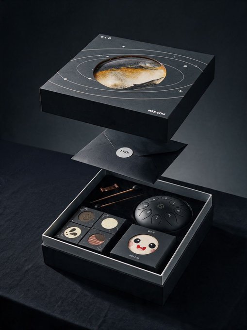 An open MSX-branded black gift box with a planetary design on the lid reveals a Mid-Autumn Festival assortment including four decorated moon cakes, a small wooden fish percussion instrument, a black teapot, and a cute MSX mascot figurine labeled "PETS CAP." The "MSX" logo is prominently displayed on both the inner lid and the outer packaging.