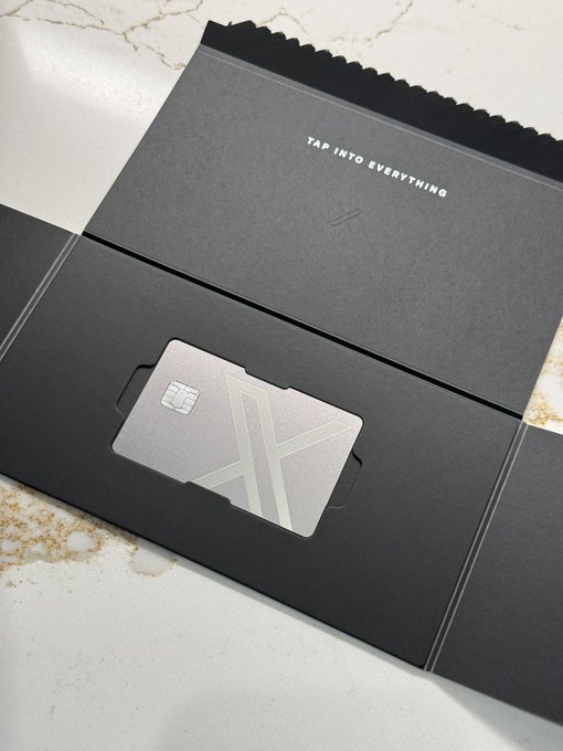A sleek black unboxing envelope reveals a premium metallic card with an embossed "A" logo and embedded chip, accompanied by the tagline "TAP INTO EVERYTHING" — a minimalist reveal that pairs perfectly with the curious "Oh?" reaction, hinting at an intriguing new tech or fintech product launch.
