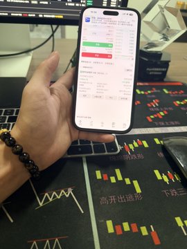 A hand holds an iPhone displaying a stock trading app over a desk mat covered in candlestick charts, with the user appearing to prepare to enter a long position near the 63,000 level after a recent pullback. The phone screen shows detailed order entry fields and chart indicators referencing the 63k price zone mentioned in the post.