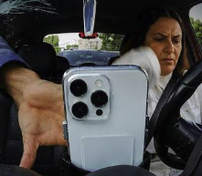 A woman takes a selfie in her car while holding up her iPhone, illustrating her point about smartphones being a major security vulnerability and the weak link in two-factor authentication systems.