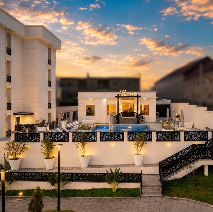 A luxurious hotel or resort with a rooftop pool, white architecture, decorative railings, and potted plants, captured at sunset with colorful clouds.