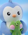 A small plush penguin toy hugging a smiling green frog plushie against a blurred light blue background.