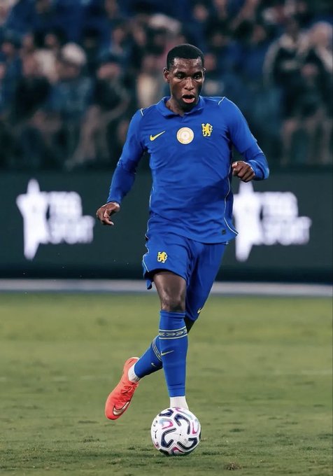 A soccer player wearing a blue Chelsea jersey with a lion crest dribbles a colorful ball on the pitch, fitting the context of Nicolas Jackson's potential £65m transfer from Chelsea to Aston Villa or Atlético Madrid.
