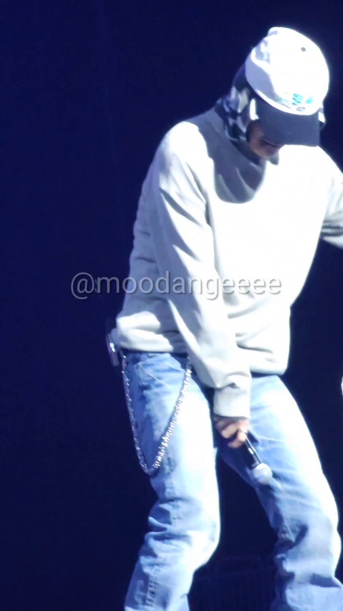 The image features a person wearing a white hat, blue jeans, and a gray sweatshirt while standing on stage with their leg extended outwards. The background of the photo is dark, which contrasts with the person's attire and emphasizes them as the main subject in the picture. There are also some text elements present in the image that read "260612 LEO for day1 fancon soundcheck! Cinnamon shake!!". This suggests that the photo was taken at a concert or event where the person is performing, possibly as part of a live performance or a promotional campaign related to the event.