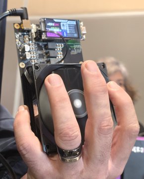 A close-up of a hand wearing a ring while holding an exposed electronic device with circuit boards and a small screen, possibly a custom gaming or tech prototype.
