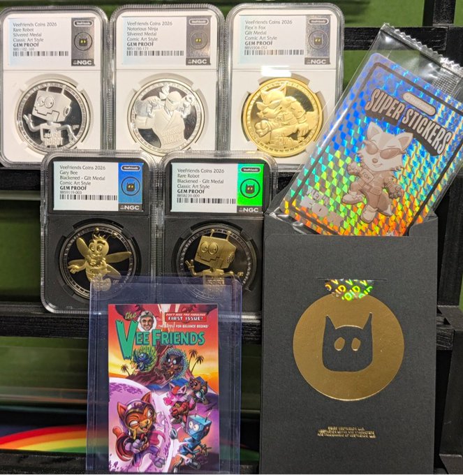 A collection of Veefriends Coins 2026 NFT items including silver Rare Robes, Silvered Metal, Flex'n Fire, gold-colored Rare Robes, gold Rare Bee, Rare Roast silver coins, a Super Stickers pack, and a Vee Friends comic book with a cat logo box.