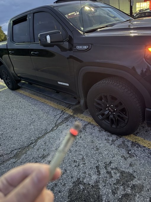 A hand holds a spent shotgun shell in front of a black GMC Sierra pickup truck parked at dusk.