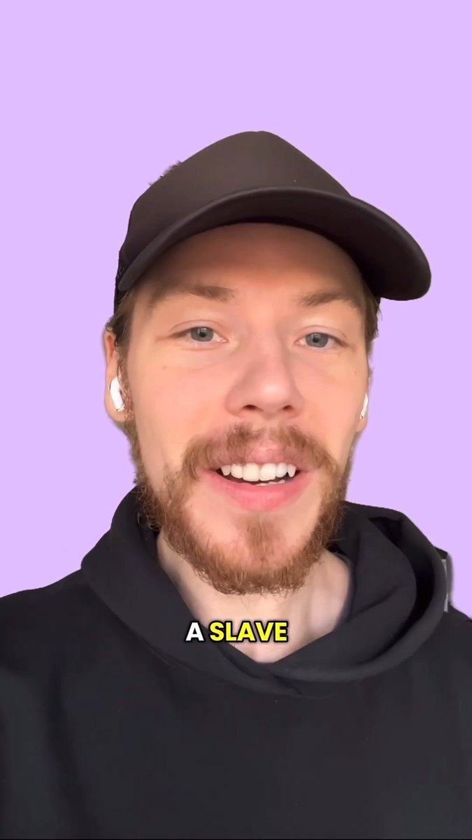MrBeast wearing a black hat and hoodie, smiling at the camera with the caption 'A SLAVE' and white earbuds.