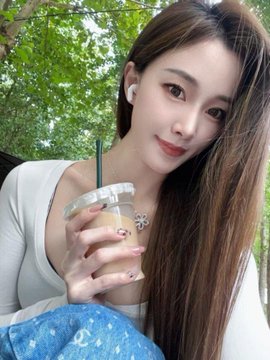 A young woman with long brown hair poses outdoors holding an iced coffee drink, wearing white earbuds and a delicate snowflake necklace. The caption suggests the photo showcases her post-celebration glow, questioning whether a 3,000-peso or won item was worth the splurge.