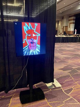 A digital display on a stand shows a colorful cartoon dog wearing sunglasses, set up in what appears to be a conference room or ballroom.