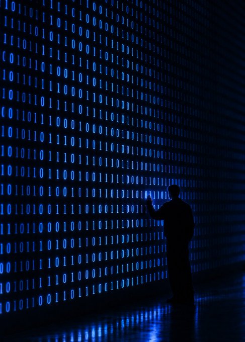 A silhouetted figure stands before a massive glowing wall of cascading blue binary code, reaching toward the stream of 0s and 1s as if rewriting them. The scene visually echoes the post's theme of "The future is written onchain," depicting the programmer as an architect shaping the digital ledger of tomorrow, one line of code at a time.