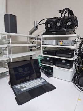 A laptop sits open on a desk in front of shelving units stacked with multiple computer servers and cooling fans, showing a media streaming or transcoding setup.