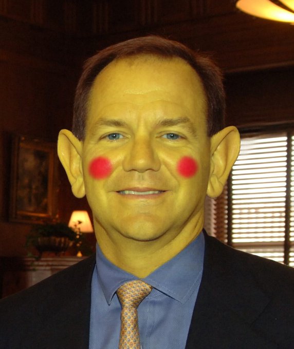 The image shows a man in a suit and tie, humorously edited to have a bright yellow tint, large pointed ears, and red rosy circles on his cheeks, resembling a cartoon character or clown. The accompanying post is a satirical quote attributed to "Tau Puter Jones," a fictional character, poking fun at financial trading culture.