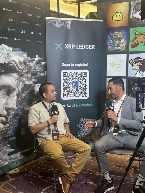 Two men are being interviewed at an XRP Ledger / Swell Hackathon event, seated in front of a banner displaying a QR code to register and NFT artwork.