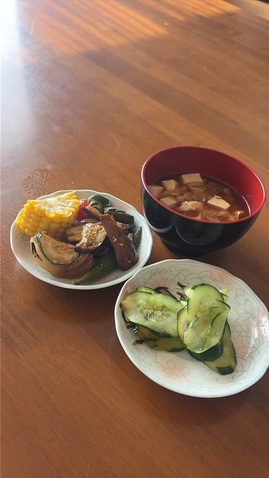 A traditional Japanese meal on a wooden table featuring miso soup with tofu, a side of corn and vegetables, and a bowl of cucumber salad.