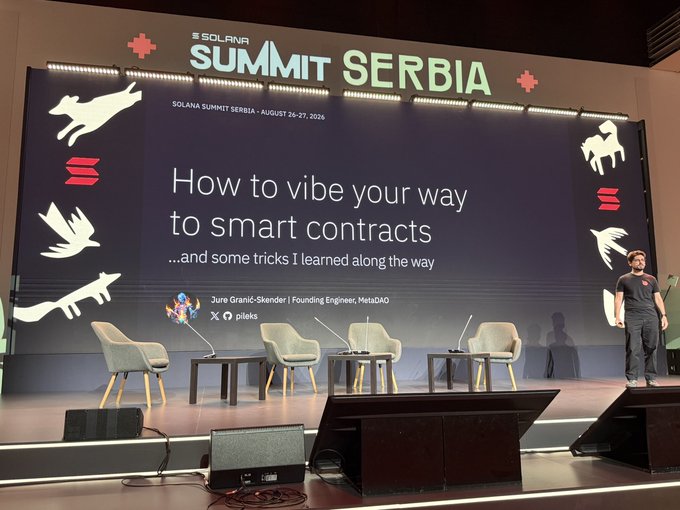 A presentation at the Solana Summit Serbia (August 26-27, 2025) on stage with a slide titled 'How to vibe your way to smart contracts...and some tricks I learned along the way' by Jure Ganič-Skender, Founding Engineer at MetaDAO.