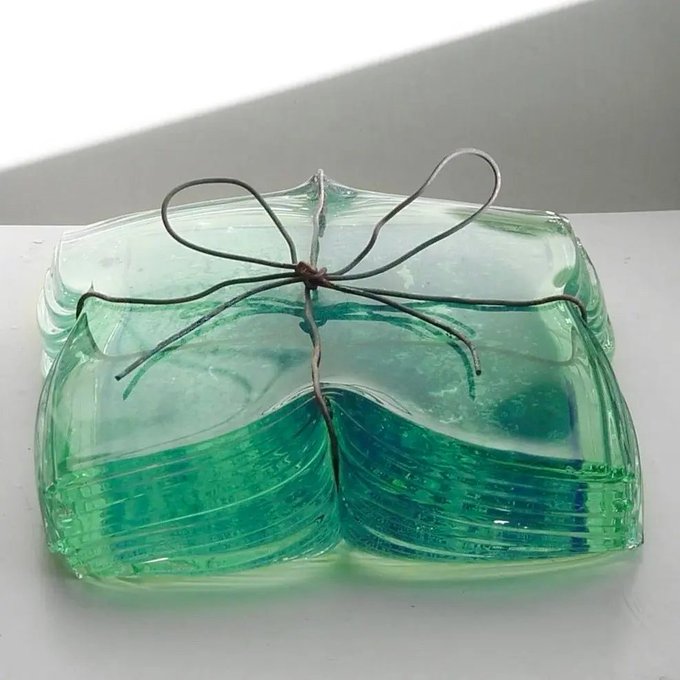 A decorative glass art piece consisting of stacked green glass plates tied together with a wire bow, sitting on a white surface.