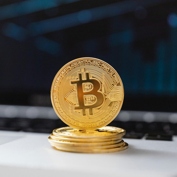A stack of gold Bitcoin tokens rests on a laptop keyboard, with one coin standing upright displaying the iconic "₿" symbol and inscriptions including "BITCOIN DIGITAL DECENTRALIZED PEER TO PEER" and "FINE COPPER." The image visually reinforces the post's message about the challenges of accurately measuring Bitcoin's onchain transfer values across the blockchain.