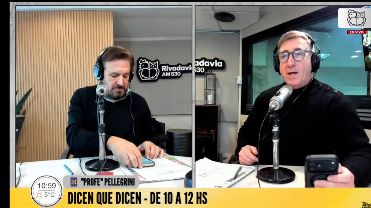 The image shows two men sitting behind microphones, each holding a cell phone. They are engaged in a conversation or discussion related to Bitcoin, possibly discussing its value or market trends. The background of the image features a clock that reads 10:50, indicating the time for their broadcast.