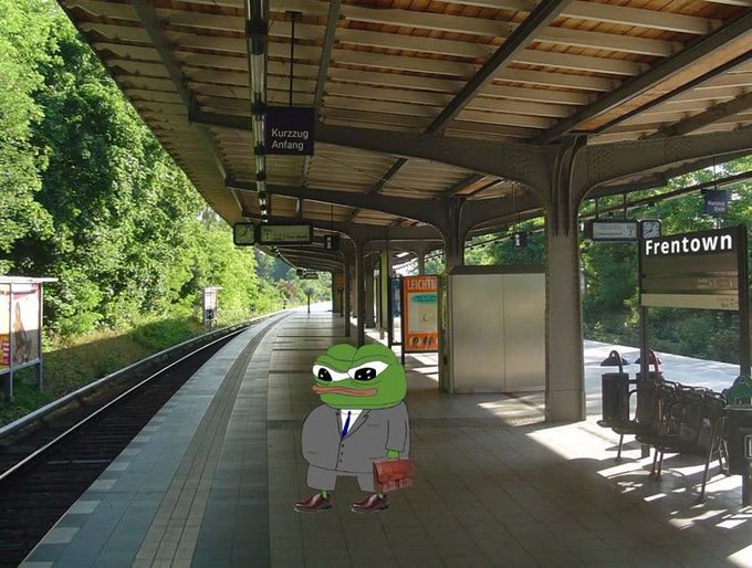 A Pepe the Frog character wearing a suit and carrying a briefcase stands on a train platform with signs reading 'Kurzzug Anfang' and 'Frentown'.
