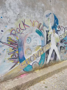 Street art/graffiti on a wall reading 'Never Rock You' and 'SHOW ME' with colorful splashes and a stylized figure holding a guitar.