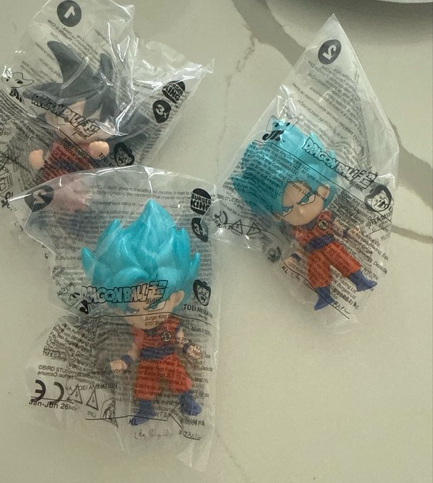 Three Dragon Ball Z toy figures in plastic packaging, including Super Saiyan Blue Goku, sitting on a light countertop.