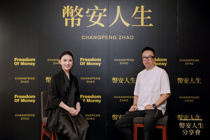 Two people seated in front of a black backdrop featuring gold text that reads '常安人生 CHANGPENG ZHAO' and 'Freedom Of Money', suggesting a promotional or interview event.