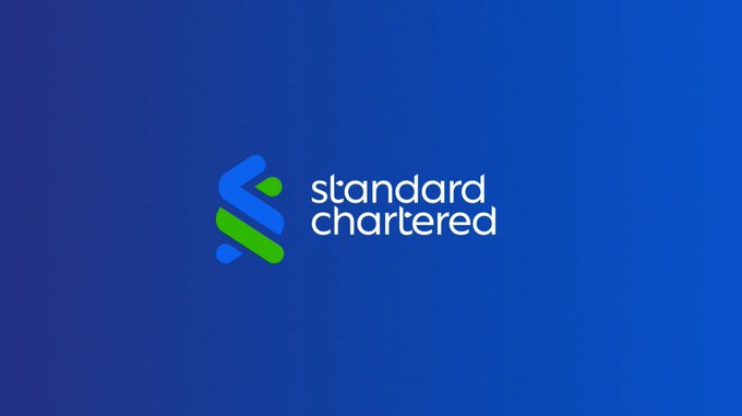 The image displays the Standard Chartered bank logo, featuring its signature blue and green intertwined design alongside the white "standard chartered" text on a deep blue background. This visual ties directly to the post's discussion of Standard Chartered's bullish Bitcoin forecast, highlighting the bank's role in shaping institutional perspectives on cryptocurrency and global liquidity trends.