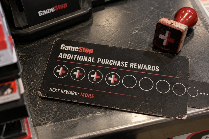 A GameStop store counter displaying a well-used 'Additional Purchase Rewards' punch card with several stamps filled in and a wooden stamp nearby.