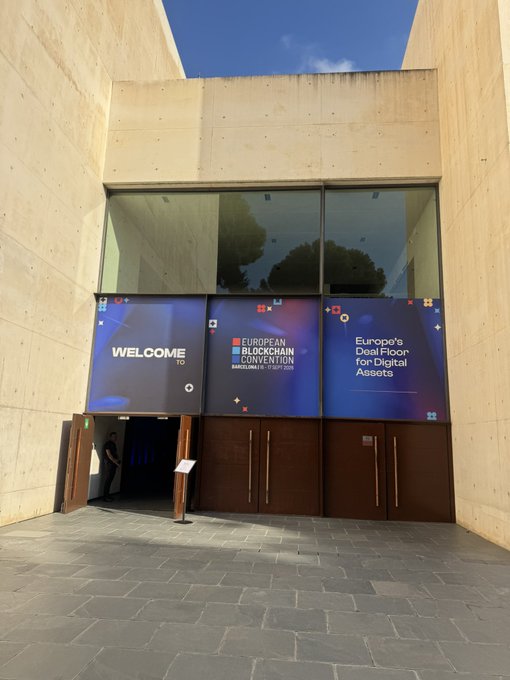 The entrance to a building featuring large banners for the 'European Blockchain Convention' with the message 'WELCOME TO Europe's Deal Floor for Digital Assets'.