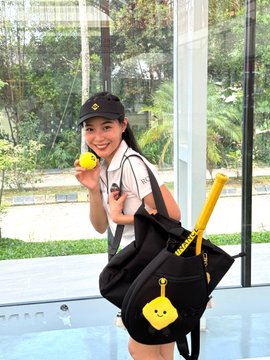 A young woman in a black cap and white top poses with a tennis ball and a black backpack, playfully holding the ball near her face in what appears to be an indoor space with greenery visible through the windows. The image ties into the post's metaphor by visually pairing tennis (where selective ball-chasing is key) with trading discipline—drawing a parallel between an athlete's focused training mindset and a trader's selective, repetitive approach to spotting real opportunities rather than chasing every price movement.
