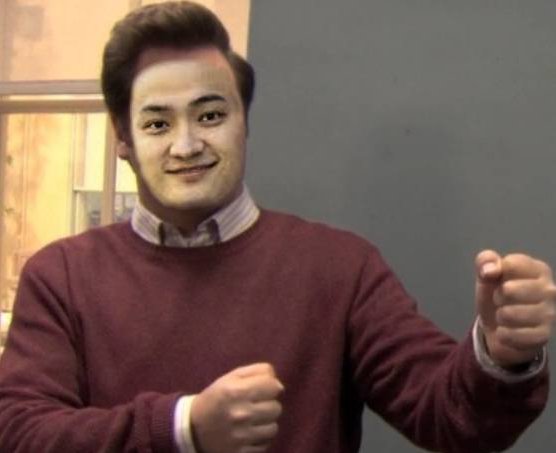 Portrait of a smiling young Asian man wearing a maroon sweater over a collared shirt, posing with his fists raised.
