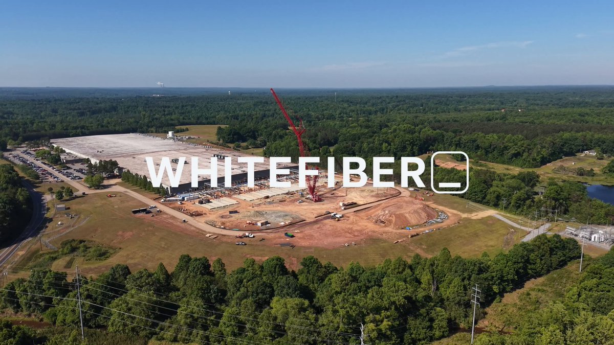 The image shows an aerial view of a construction site, with a crane visible in the background. The text "Whitefiber" is written above the crane, indicating that this project belongs to Whitefiber. The caption below the image provides information about the progress of the construction project and the role of the crane in completing it.