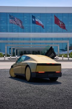 A yellow Tesla Cybertruck parked in front of a glass building displaying American, Texas, and another flag.
