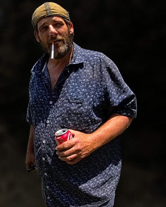 A bearded man wearing a bandana and patterned shirt holds a Coca-Cola can and has a cigarette in his mouth. The rugged, gritty appearance of the man fits the meme-style vibe often used to promote meme coins like $PENIX, with the casual outdoor aesthetic adding to the irreverent tone of the Solana coin launch celebrating "Mr. Penix."