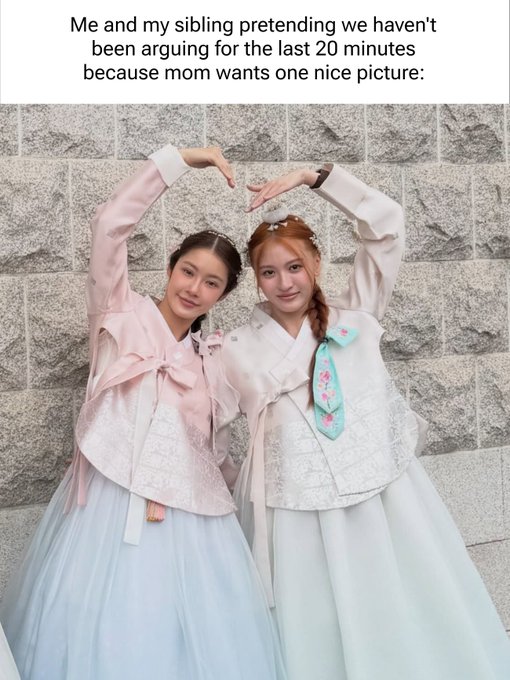 Two women in traditional pink and white hanbok dresses pose together, raising their arms to form a heart shape above their heads against a stone wall. The caption reads: "Me and my sibling pretending we haven't been arguing for the last 20 minutes because mom wants one nice picture."